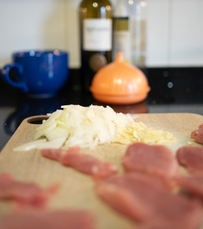 Sliced pork tenderloin, chopped onions, and minced garlic sit on a wooden cutting board in a modern kitchen, ready for cookingの写真素材