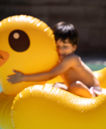 Young child hugging a large inflatable duck in a sunny pool