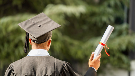 Graduate student holding university diploma wearing graduation gown and capの写真素材
