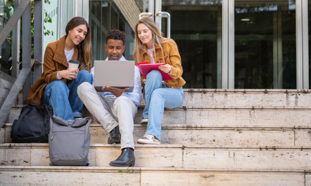 Group of diverse university students collaborating on a project, using laptop and taking notes, enjoying coffee during study break outdoorsの写真素材