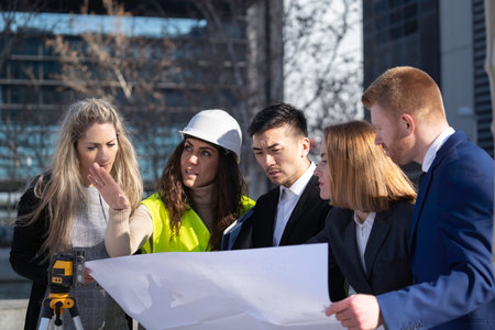 Diverse team of engineers and architects reviewing blueprints on a construction site, collaborating on a projectの写真素材