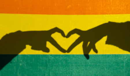 Shadow of two hands forming a heart shape over lgbtq+ rainbow flag, symbolizing love, acceptance, and prideの写真素材