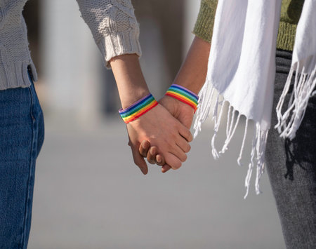 Two women holding hands, wearing rainbow bracelets, symbolizing lgbtq+ pride, love, and unityの写真素材