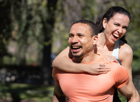 Couple having fun piggybacking in a park, enjoying a sunny day outdoorsの写真素材