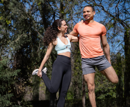 Smiling sportspeople stretching legs together after exercising in park on a sunny day