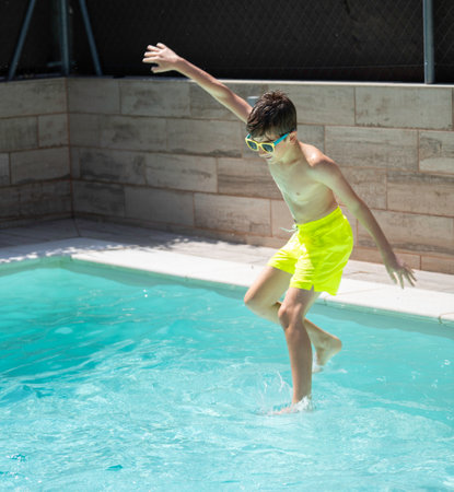 Young boy carefully entering a swimming pool on a hot summer day, enjoying his vacationの写真素材