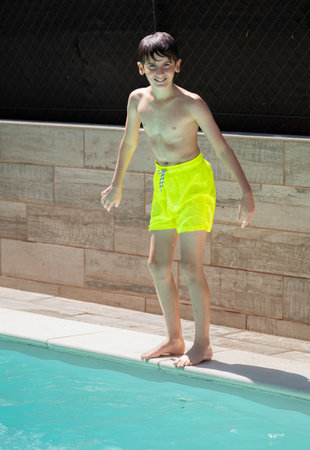 portrait of young boy standing at the edge of a pool, ready to jump inの写真素材
