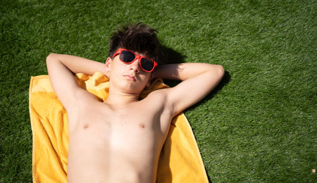Young teenager man sunbathing on a yellow towel in green grass wearing red sunglasses with copy spaceの写真素材