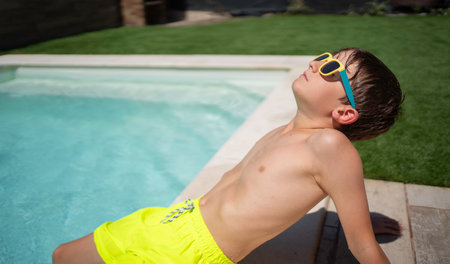 Side view of young boy in sunglasses relaxing enjoying a sunny day by the pool with copy spaceの写真素材