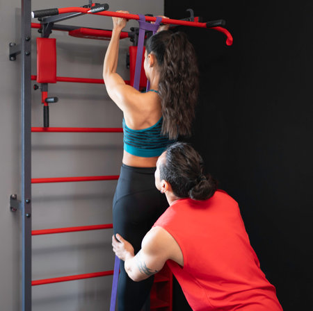 Sporty woman exercising with resistance band and personal trainer assisting her during pull-ups workoutの写真素材