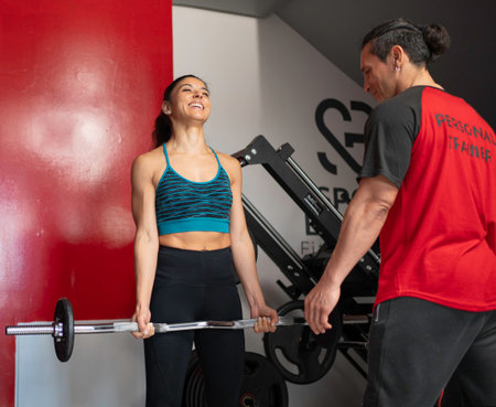 Happy sportswoman lifting weights with the help of her personal trainer in a modern gymの写真素材