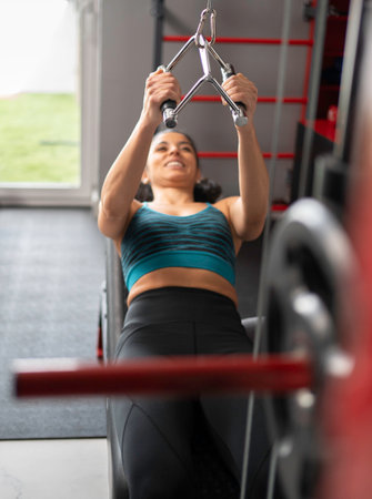 Smiling woman lifting weights on a cable row machine, strengthening her back musclesの写真素材