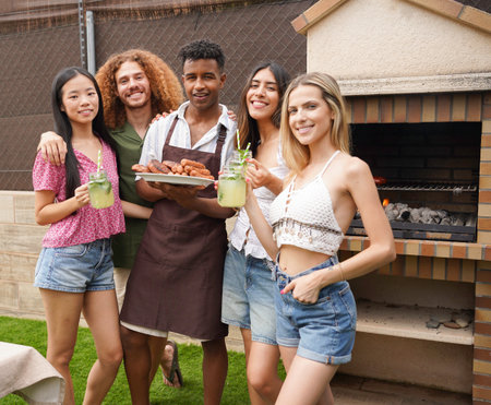 Cheerful young friends enjoying refreshing drinks and delicious barbecue food, celebrating summer in the backyardの写真素材