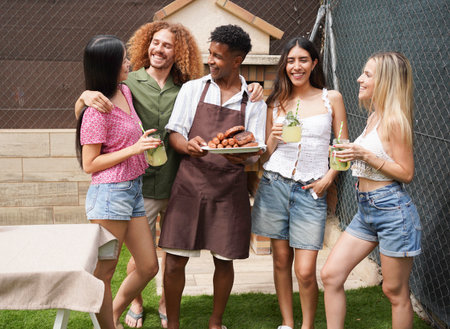 Chef showing grilled sausages and burgers to friends enjoying drinks at barbecue partyの写真素材