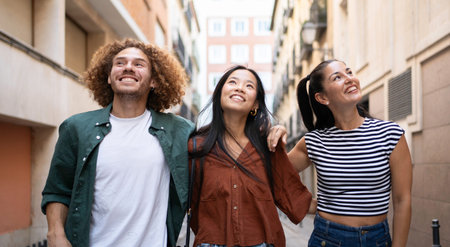 Three happy multi-ethnic friends are walking down the street and looking up at the buildings