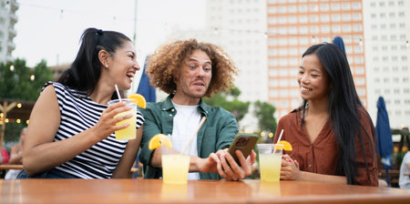 Three friends are laughing and enjoying refreshing drinks at an outdoor cafe, sharing a moment of...