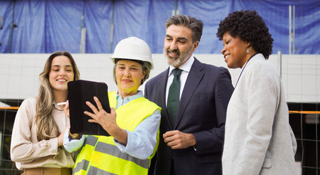 Diverse group of construction professionals collaborating on a project, using a digital tablet at a building siteの写真素材
