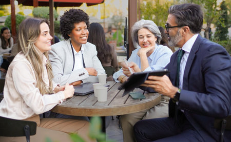 Business colleagues discussing work during a meeting at an outdoor cafe, using a digital tablet for...