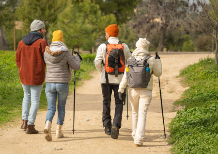 Rear view of four hikers are enjoying a scenic nature trail, walking on a dirt path with backpacks and trekking polesの写真素材