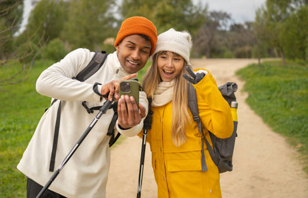 Happy multiethnic couple of hikers taking selfie with smartphone fixed to a stick during nordic...