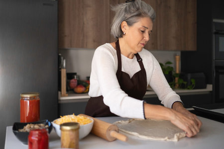 Senior woman stretching pizza dough on a kitchen counter for a homemade meal