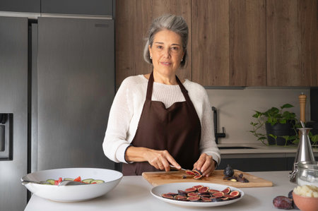 Senior woman wearing apron, slicing fresh figs for a healthy salad on kitchen counterの写真素材
