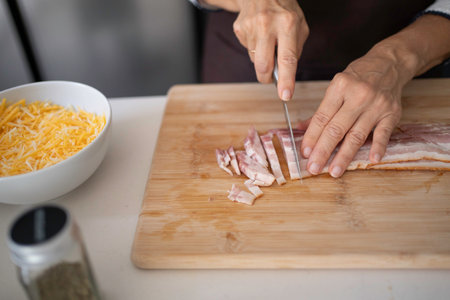 Hands chopping raw bacon strips on a wooden cutting board with a knifeの写真素材