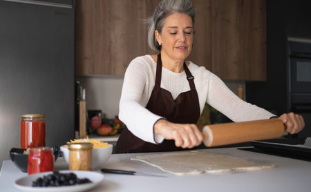 Woman in apron preparing homemade pizza dough with a rolling pin