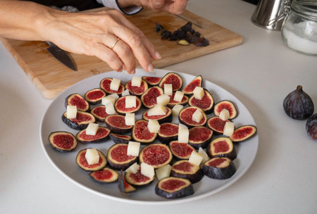 Hand placing cheese cubes on sliced fresh figs for an appetizerの写真素材