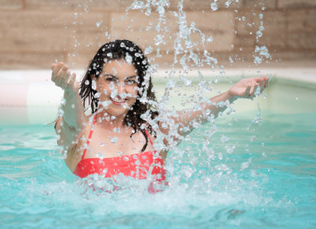 Female splashing water in blue swimming pool, enjoying summer vacationの写真素材