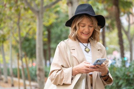 Smiling senior woman using smartphone in urban park, connected with technology with copy spaceの写真素材