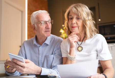 Senior couple discussing financial plans, managing budget, and reviewing documents at homeの写真素材