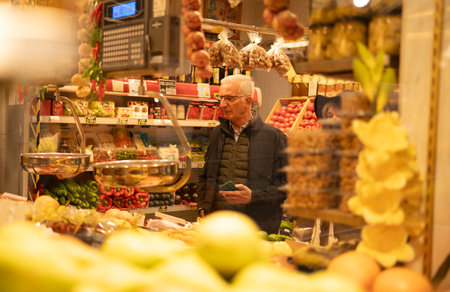 Senior man with glasses holding a smartphone while shopping for fresh produce in a grocery storeの写真素材