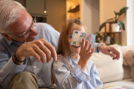 Grandfather giving a 20 euro banknote to a smiling granddaughter, teaching about financeの写真素材