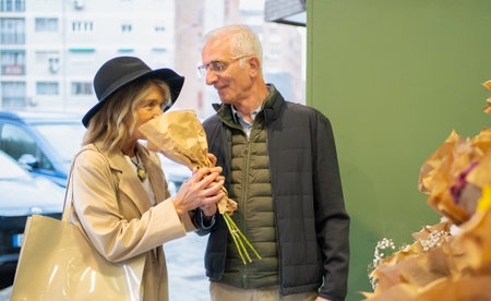 Senior woman smelling a fresh bouquet, while her husband looks on fondly during a dateの写真素材
