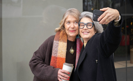 Two cheerful mature friends smiling, capturing moments together with a mobile phone