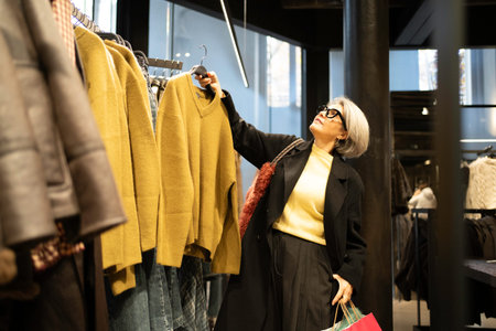 Woman browsing clothing rack while holding a shopping bag in a modern boutiqueの写真素材