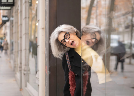 Senior woman with gray hair and eyeglasses peeking from a shop window, expressing surprise
