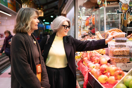 Two mature women choosing nuts and apples at a vibrant indoor marketの写真素材