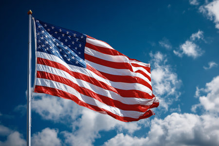 American flag gracefully waving against a bright blue sky with white clouds