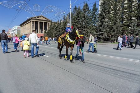 Little boy rides on a smart brown horse driven by young man along the avenue of Krasnoyarsk city during the celebration of Victory Day WWII.のeditorial素材