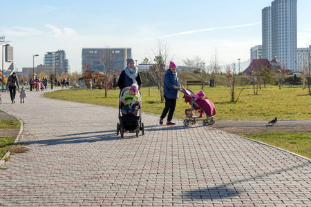 Young mothers walk with small children in a public garden, on the background of the Krasnoyarsk...