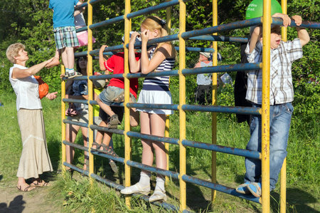 Children climb the sports ladder on the playground against the background of green trees on a sunny...