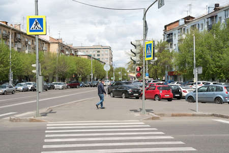 A guy walks along the sidewalk before a pedestrian crossing on a street on a spring day. Krasnoyarsk. Russia.のeditorial素材