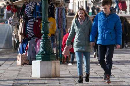 Venice. Italy Young couple walks along a clothing store on the central promenade of Riva degli Schiavoni in a winter sunny day.のeditorial素材
