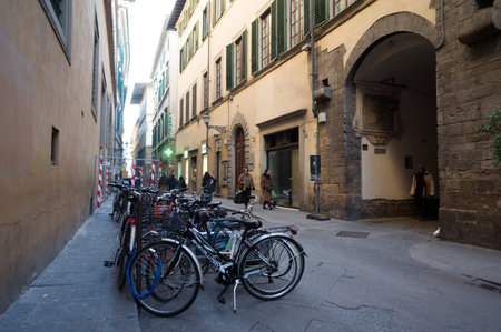 Florence, Italy. Bicycles stand on the bike stand on a narrow street with pedestrians and ancient architecture.のeditorial素材