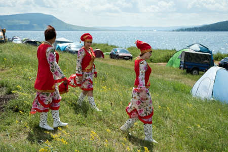 Women in Tatar folk costumes walk along the lake with tents at the Karatag music festival. Krasnoyarsk region.のeditorial素材