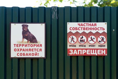 Signs with threatening and prohibiting inscriptions - no entry, the territory is guarded by a dog - on the metal fence of a private site.のeditorial素材