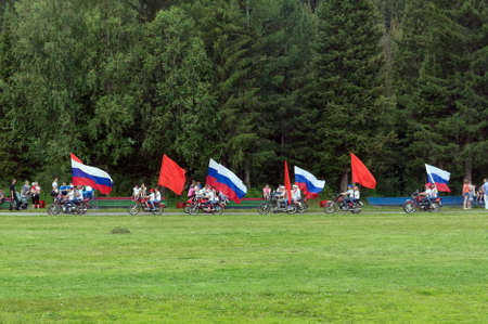 Motorbikes with red and Russian flags ride past spectators on the background of coniferous forest in the stadium.のeditorial素材