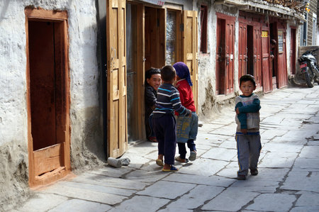 Children of Tibetan ethnicity play on the cobbled sidewalk of a city street on a sunny day. Jomsom,...